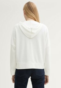 Hoodie blanc avec une texture douce, épaules tombantes et une capuche. Affiche un design décontracté avec une coupe raccourcie et un ourlet côtelé.