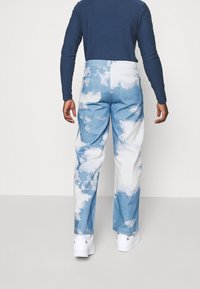 Ljust blå denimbyxor med ett molnmönster och vita accenter. De har en avslappnad passform och är kombinerade med vita sneakers.