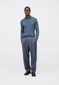 Long-sleeve polo in teal, paired with light grey pleated trousers. Smooth fabric, fitted design, and black dress shoes complete the look.