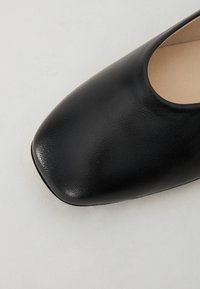 Chaussure en cuir noir avec un bout arrondi et une texture lisse. La tige présente un design bas et des détails minimalistes.