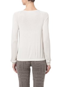 Helle langärmlige Bluse mit lockerer Passform, dehnbarem Material, gerafftem Saum und Raglanärmeln. Ansicht von hinten.