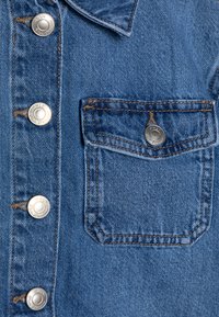 Jeans jakna v svetlo modri barvi, s kovinskimi gumbi, prsno žepom s kontrastnim šivom in zaobljenim pokrovom.