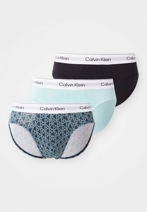 Three pairs of Calvin Klein briefs: one black, one mint green, and one patterned navy blue with a geometric design and white waistband.