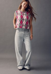 Colorful argyle knit sleeveless sweater with pink, gray, and white hearts, paired with light gray wide-leg jeans and gray slip-on shoes.