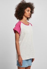Rövid ujjú póló világosszürke testtel és rózsaszín raglán ujjal. Puha pamut keverék anyag, laza szabással és lekerekített nyakkivágással.