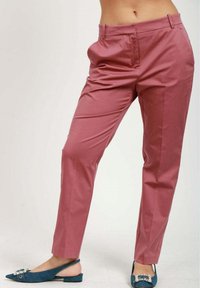 Rosaröda byxor med skräddarsydd passform, mjuk textur och framfickor. Modellen kombinerar dem med blå, spetsiga slingback-sandaler.