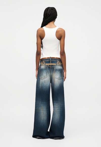 Γυναίκα με μακριά πλεξούδα, που φοράει λευκό αμάνικο τοπ και φαρδιά ξεθωριασμένα μπλε τζιν με κεντημένο λογότυπο "DSQUARED2" στη πίσω μέση.
