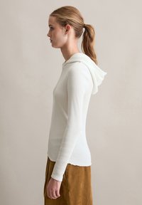 Witte geribbelde hoodie met lange mouwen, gemaakt van een zachte stof en met een ontspannen pasvorm. De hoodie heeft een afgeronde zoom en een capuchon bij de hals.