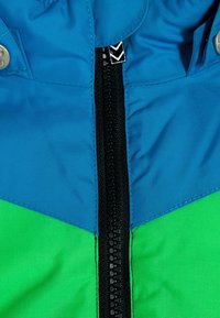 Barevná bunda s modro-zeleným designem, vyrobená z hladkého, texturovaného materiálu. Černý zip probíhá vertikálně a je doplněn stříbrnými kovovými detaily.