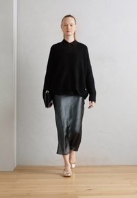 Maglione oversize nero, gonna midi nera lucida e scarpe basse chiare, con una semplice pochette. Texture lisce e design minimale.