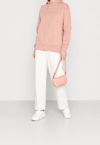 Ljusrosa hoodie med snörning, vita vida byxor och en liten ljusrosa axelväska. Vita sneakers med subtila detaljer.