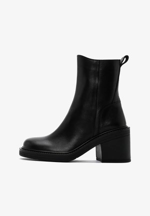 Bottines noires en cuir lisse, avec un bout arrondi et un épais talon bloc. Panneaux élastiques latéraux pour un enfilage facile.