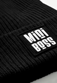 Black knit beanie with a ribbed texture and a rectangular black label featuring the white text "Mini Boss."