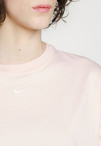Světle růžové bavlněné tričko s kulatým výstřihem a krátkými rukávy, s malým bílým logem Nike swoosh na hrudi.