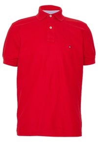 Červené bavlněné polo tričko se standardním límcem, dva knoflíky na zapínání a malým logem na hrudi. Krátké rukávy a hladká textura.