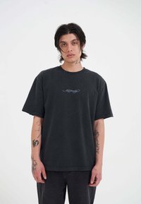 Sort bomulds oversized t-shirt med rund halsudskæring og uferdige ærmekanter, prydet med blå logo-broderi på brystet.