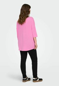 T-shirt oversize rosa con maniche ampie, realizzata in tessuto morbido. Abbinata a pantaloni neri slim-fit e sneakers nere con accenti bianchi.