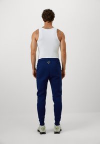 Marinesweatpants med indsnævrede ben og elastiske manchetter, med en baglomme og logo-detail. Sættes sammen med en hvid tank top og sko.