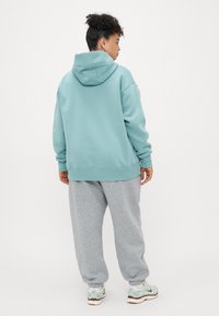 Moletom azul claro com um capuz grande e punhos canelados, emparelhado com calças de moletom cinzentas. O conjunto apresenta um ajuste descontraído e uma textura suave.