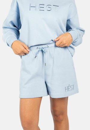 Lys blå genser og matchende shorts med snor i livet, begge med "HÉST" brodert i hvit tråd.