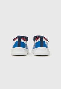 Zapatillas deportivas azules y blancas con parte superior de malla y sintético, correas elásticas y una suela blanca acolchada. La vista trasera muestra el diseño del talón.