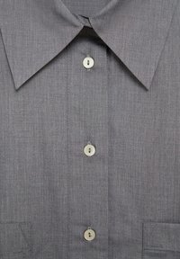 Chemise grise à col avec trois boutons blancs visibles sur le devant et un tissu à texture subtile.