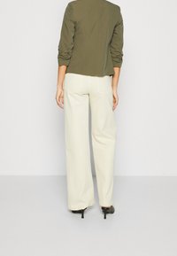 Zielony oliwkowy marynarka dopasowana z lekko skróconym krojem, w połączeniu z kremowymi spodniami w szerokiej nogawce i czarnymi szpilkami.