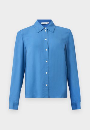 Modrá košeľa s dlhým rukávom zapínaná na gombíky, so špicatým golierom a bielymi gombíkmi, zobrazená na jednoliatom pozadí.