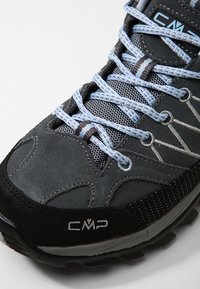 Grau Wanderschuh mit einem Obermaterial aus Wildleder und Mesh, blauen Schnürsenkeln, schwarzer Gummisohle und einer verstärkten Zehenkappe. Das Logo ist an der Seite aufgedruckt.