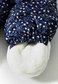 Tissu matelassé bleu marine avec petits motifs floraux roses ; doublure en peluche blanche douce apparente au niveau du poignet ; bordure élastiquée.