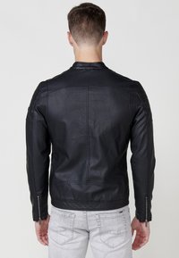 Chaqueta de cuero negra con un diseño ajustado, acabado texturizado, puños con cremallera y herrajes mínimos. Incluye detalles de costura vertical.