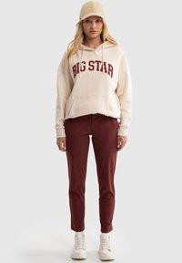 Bežs kapucis ar "BIG STAR" logo bordo krāsā, apvienots ar bordo krāsas pieguļošām biksēm un baltām kedām, papildināts ar bežīgu cepuri.