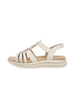 Sandale beige à bout ouvert avec des sangles élastiques et des boutons décoratifs, présentant une semelle intérieure rembourrée et un talon compensé bas avec des accents blancs.
