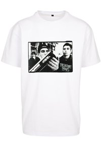 Fehér pamut póló, fekete-fehér grafikával három egyénről, akik egy készüléket használnak. A szöveg fekete színben olvasható: "Beastie Boys".