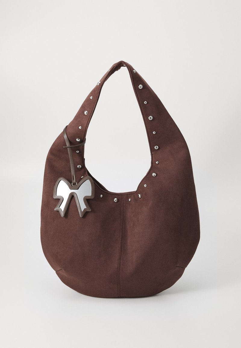 Sac hobo en daim marron avec des clous argentés le long du bord supérieur et un charm en forme de nœud métallique accroché à la sangle. Large ouverture et texture douce.