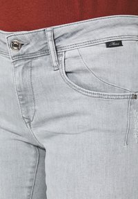 Ljusgrå denimjeans med slät struktur, femfickorsdesign och knappstängning; har en liten svart varumärkesetikett på midjebandet.