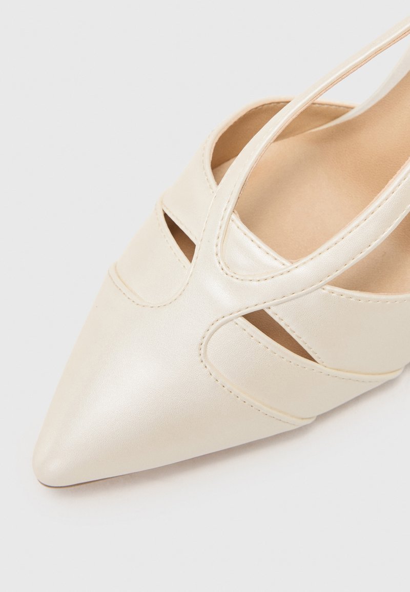 Scarpa in pelle beige con design a punta, caratterizzata da dettagli ritagliati lungo i lati e una superficie liscia.