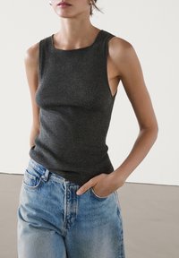 Canottiera a costine grigio scuro con scollatura quadrata, abbinata a jeans chiari a vita alta, che mettono in risalto una silhouette sagomata e un tessuto texture.