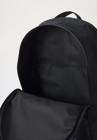 Zwarte stoffen rugzak met een ritssluiting, die een glad interieur toont. Kenmerken zijn onder andere een hoofdcompartiment en een voorvak.