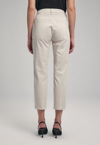 Pantalons beige ajustés avec une coupe slim, longueur raccourcie et poches arrière, associés à des sandales à talons noirs. Texture de tissu lisse.