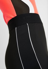 Jupe noire à taille ajustée, avec des coutures blanches contrastantes. Le haut présente un design en maille corail vif et noir.