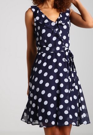 Abito blu navy a pois bianchi, con scollatura arricciata, senza maniche e cintura annodata in vita. Tessuto leggero e fluido.