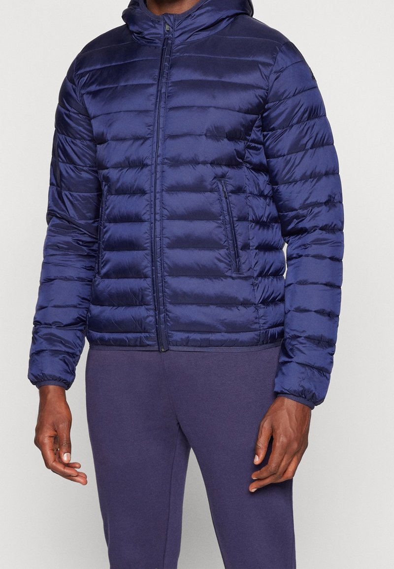 Marine pufferjack met capuchon, geborduurd textuur, voorrits en zijzakken. Beschikbaar met elastische manchetten en een getailleerd ontwerp.