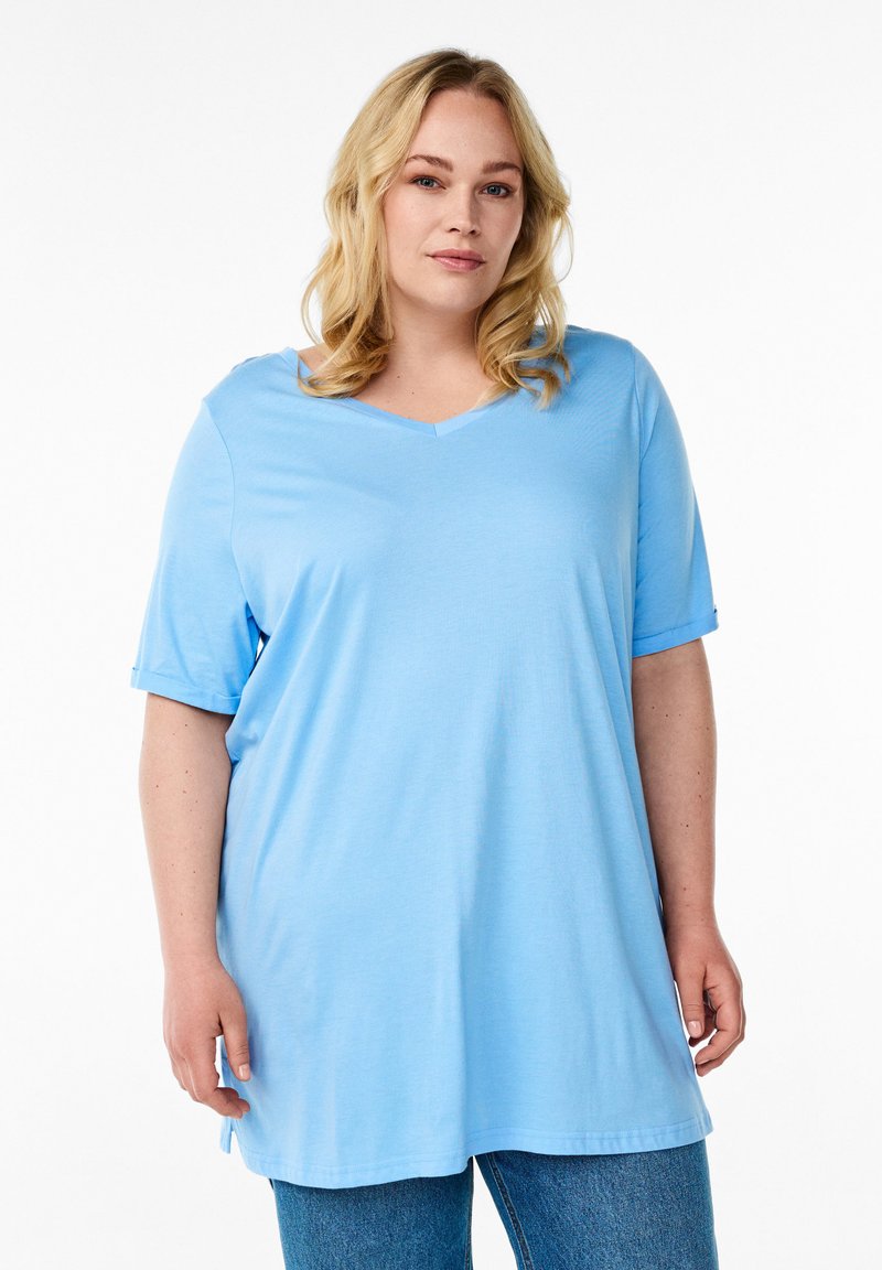 Camiseta de cuello en V de color azul claro con mangas cortas y un corte relajado. Tejido suave, con aberturas laterales en el bajo, combinada con jeans de mezclilla azul.
