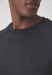 Gros plan sur une personne portant un t-shirt à col rond noir avec un petit logo Nike Swoosh noir sur la poitrine.