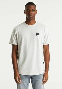 T-shirt corto a maniche corte grigio chiaro realizzato in morbido cotone. Presenta un piccolo patch logo nero sul petto e maniche arrotolate.