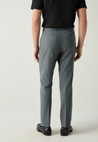 Pantalones de vestir grises con un ajuste entallado, que presentan un diseño de frente plano, costuras sutiles y dos bolsillos traseros. Combinados con zapatos negros.