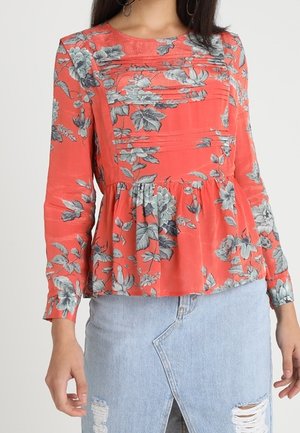 Blusa floreale color corallo con maniche lunghe, dettagli plissettati e design a peplum. Presenta motivi floreali grigi e blu sul tessuto.