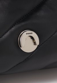 Zwarte lederen handtas met een gequilt ontwerp en een zilveren ronde sluiting met "PINKO" gegraveerd. Gladde textuur met zichtbare stiksels.