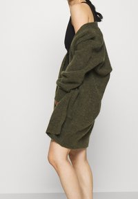 Olivgrön oversized stickad kappa med lösa ärmar och öppen front, med en mjuk textur och avspänd passform.